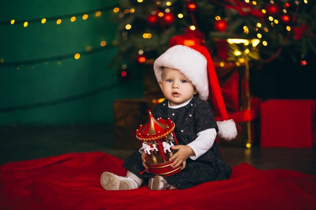 Niña sentada por el árbol de navidad con el juguete