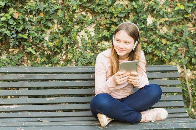 Foto gratuita niña sentada en el banco con la música que escucha del teléfono móvil en los auriculares