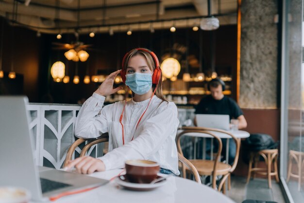 Una niña sentada en una cafetería con auriculares brote de coronavirus