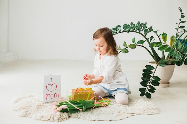 Foto gratuita niña sentada con caja de regalo y flores de tulipán