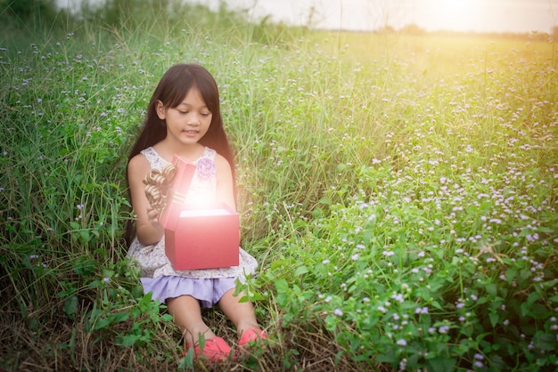 niña sentada por el campo con un regalo y mirarlo,