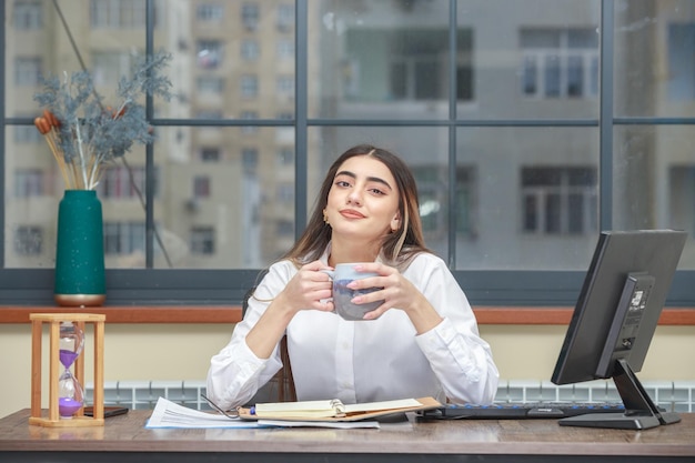 Una niña sentada detrás del escritorio y sosteniendo su taza de té Foto de alta calidad