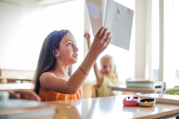 Niña sentada en el escritorio de la escuela sosteniendo el cuaderno