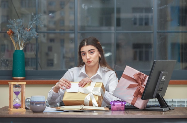 Niña sentada en el escritorio y tratando de abrir su caja de regalo