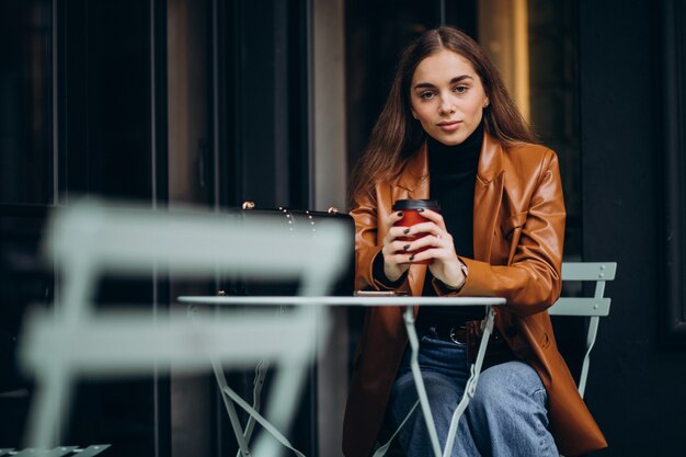 Niña sentada fuera de la cafetería y tomando café