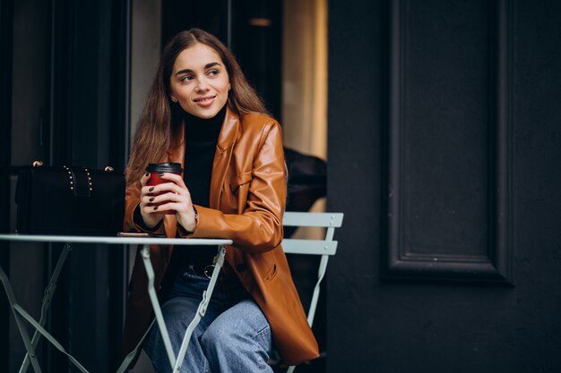 Niña sentada fuera de la cafetería y tomando café