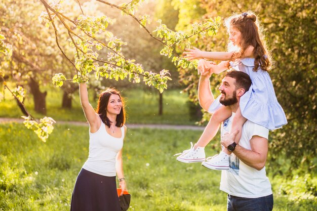 Niña sentada en el hombro de su padre recogiendo la hoja del árbol con la madre