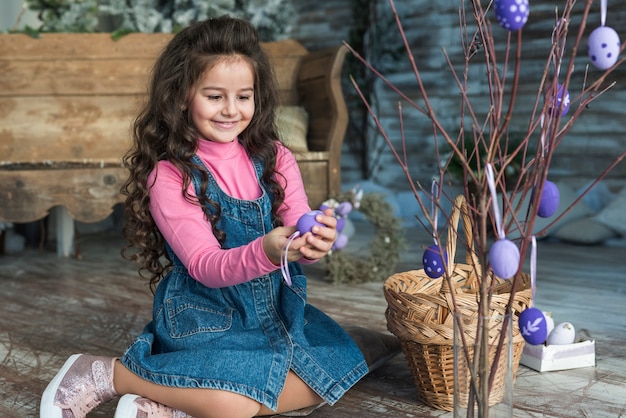 Niña sentada con huevo de Pascua cerca de ramas en florero