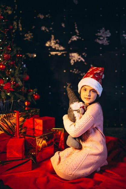 Niña sentada junto al árbol de navidad y desempaquetando regalos