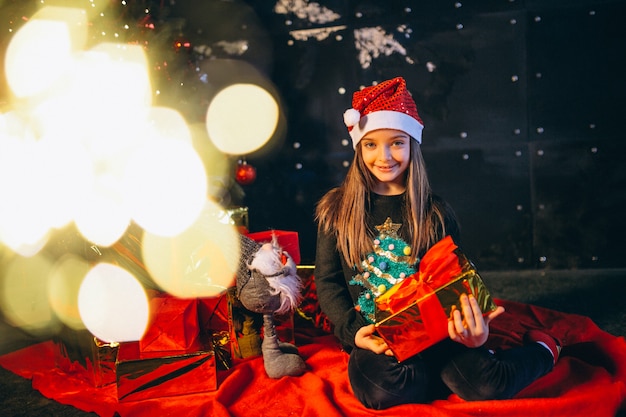 Niña sentada junto al árbol de navidad y desempaquetando regalos