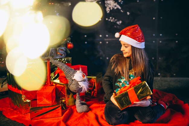 Niña sentada junto al árbol de navidad y desempaquetando regalos