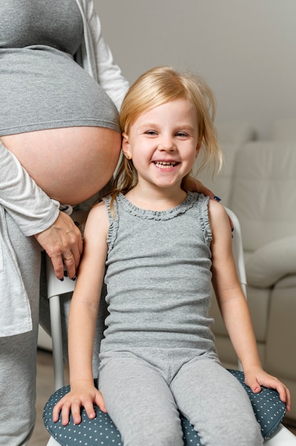 Niña sentada junto a la barriga embarazada de la madre