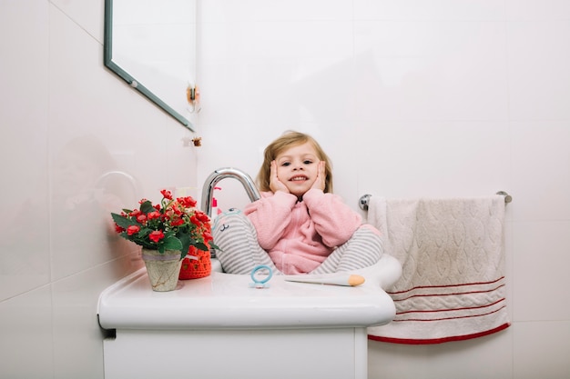 Foto gratuita niña sentada en el lavabo del baño con macetas