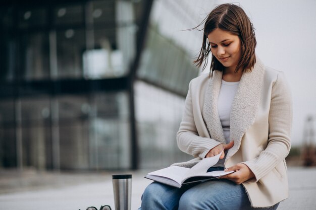 Niña sentada leyendo un libro y tomando café fuera de la calle