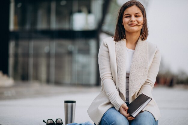 Niña sentada leyendo un libro y tomando café fuera de la calle