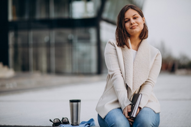 Niña sentada leyendo un libro y tomando café fuera de la calle