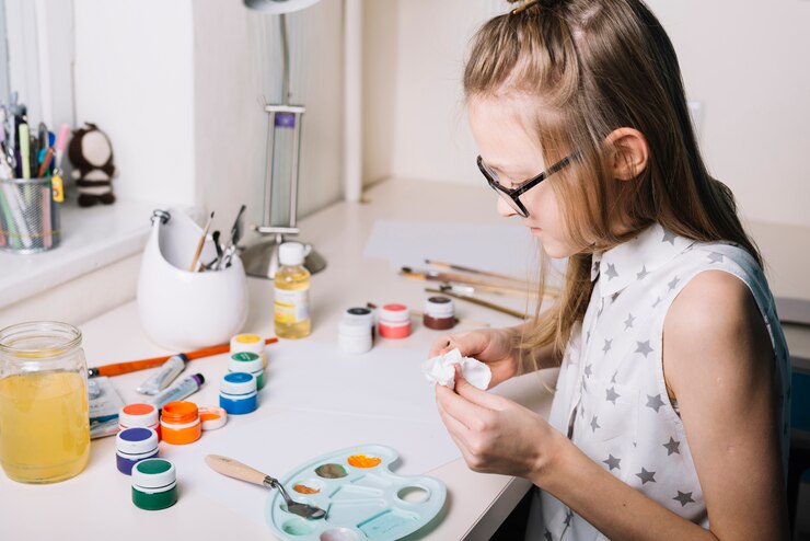 Foto gratuito niña sentada a la mesa con latas de gouache y paleta