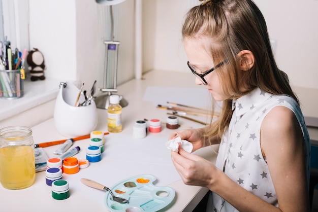 Niña sentada a la mesa con latas de gouache y paleta