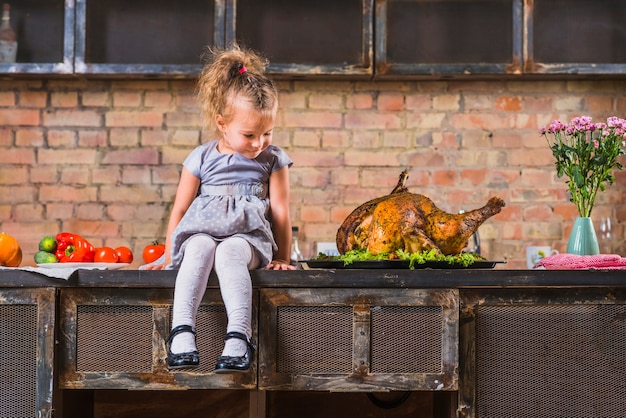 Niña sentada en la mesa con pavo al horno