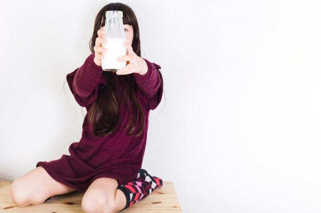 Niña sentada en el mostrador de madera mostrando la botella de leche