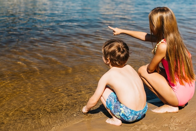 Niña sentada con un niño y apuntando a la costa