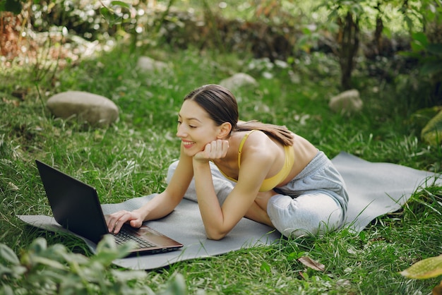 Niña sentada en un parque de verano y sosteniendo una computadora portátil en sus manos