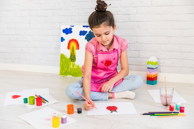 Niña sentada en la pintura del piso sobre papel blanco con colores