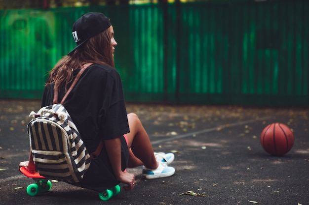 Niña sentada en plástico naranja penny shortboard sobre asfalto en la tapa