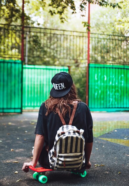 Niña sentada en plástico naranja penny shortboard sobre asfalto en la tapa