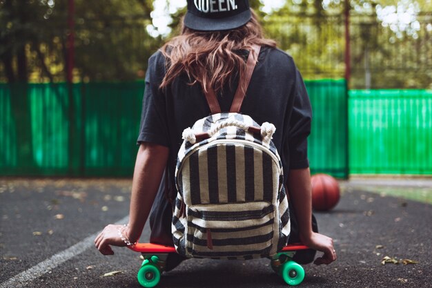 Niña sentada en plástico naranja penny shortboard sobre asfalto en la tapa