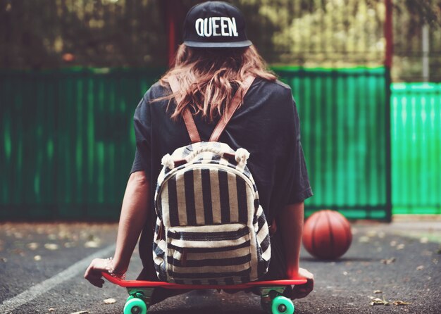 Niña sentada en plástico naranja penny shortboard sobre asfalto en la tapa