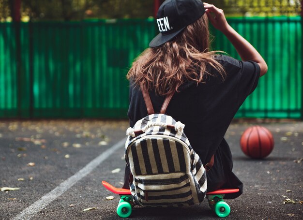 Niña sentada en plástico naranja penny shortboard sobre asfalto en la tapa