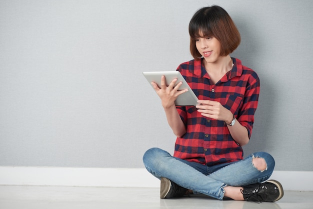 Niña sentada en postura de loto navegando por la red en su tableta digital