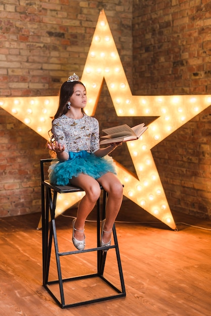 Foto gratuita niña sentada en la silla alta ensayando delante de estrella brillante contra la pared de ladrillo