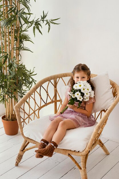 Niña sentada en un sillón con ramo de flores de primavera