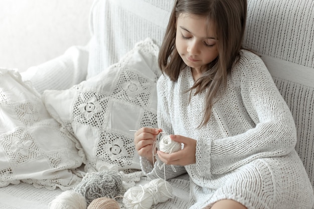 Niña sentada en el sofá con hilos, concepto de ocio en casa, crochet.