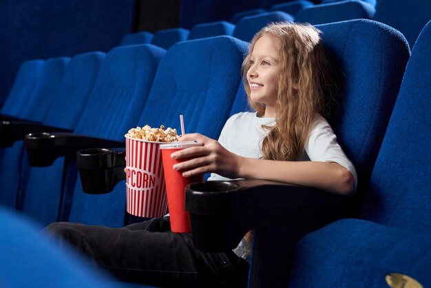 Niña sentada sola en el cine y viendo una película cómica