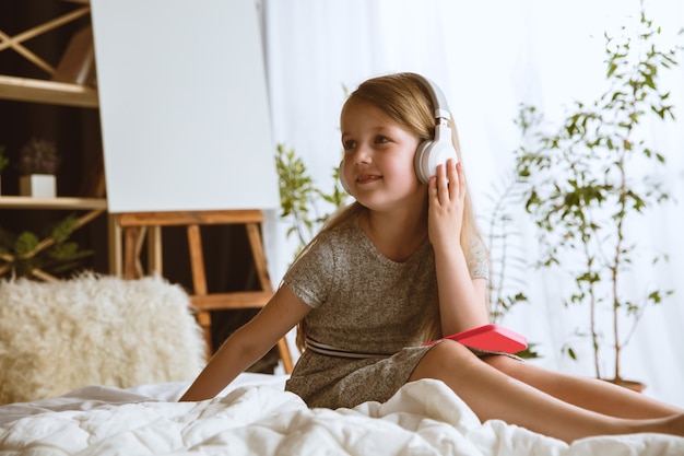 Niña sentada en su cama con grandes auriculares escuchando música favorita y disfrutando