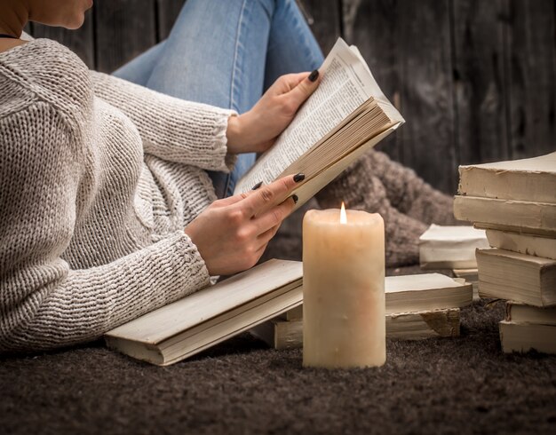 niña sentada en el suelo rodeada de muchos libros blancos y una vela grande