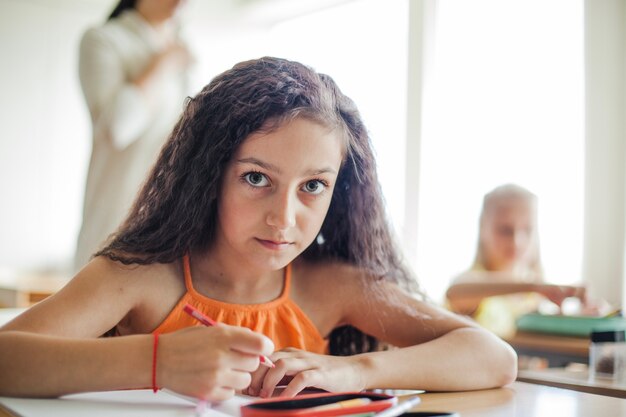 Niña, sentado, escritorio, tenencia, lápiz