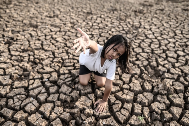Foto gratuita la niña se sentó en otra parte, con la mano hacia el cielo para pedir lluvia en el suelo seco, el calentamiento global.