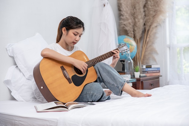 La niña se sentó y tocó la guitarra en la cama.