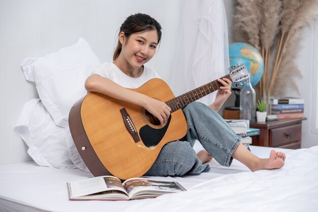 La niña se sentó y tocó la guitarra en la cama.