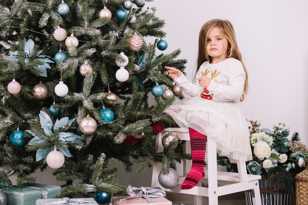 Niña en silla decorando árbol de navidad