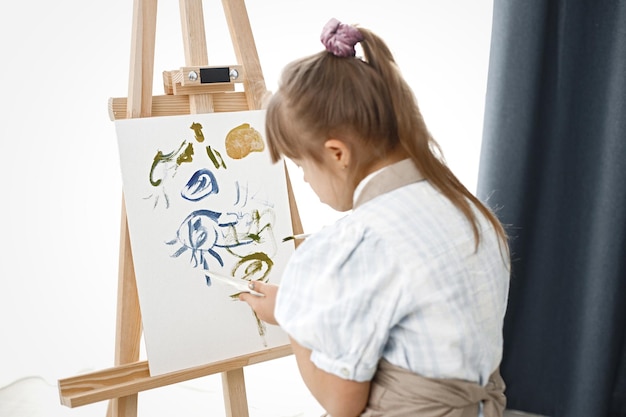 Niña con síndrome de Down con delantal beige pintando en un caballete