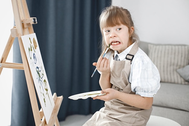 Niña con síndrome de Down con delantal beige y pintando en un caballete