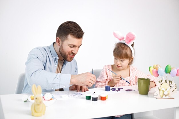 Niña con síndrome de Down y su padre pintando huevos de colores de Pascua