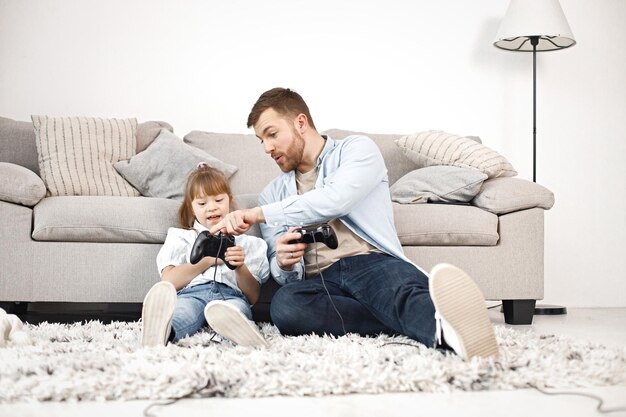 Niña con síndrome de Down y su padre sentados en el suelo y jugando PlayStation