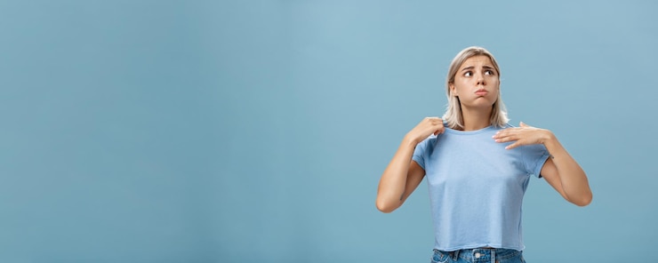 Foto gratuito niña sintiendo incomodidad por el calor de pie sobre fondo azul en fug exhalando y frunciendo el ceño mirando al sol sufriendo de calor agitando con la camiseta para refrescarse