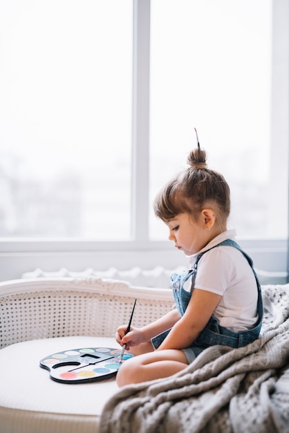 Niña en el sofá con paleta de acuarela